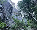 The rugged trail passes a large rock face along the Slhanay Peak Trail